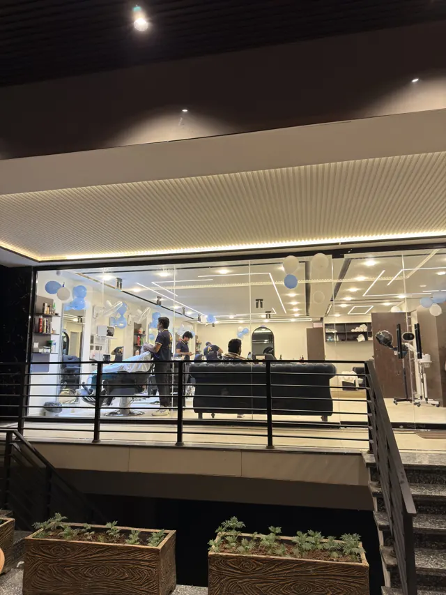 The lounge at night through the glass front, with barbers at work inside
